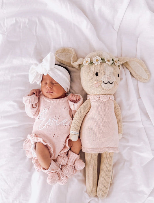 pagliaccetto BONBON rosa indossato su una neonata che dorme di fianco ad un coniglietto fatto all'uncinetto