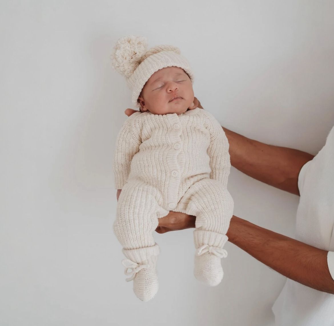 bimbo con indosso il nostro set latte composto da tutina, cappellino e babbucce in cotone organico testurizzato